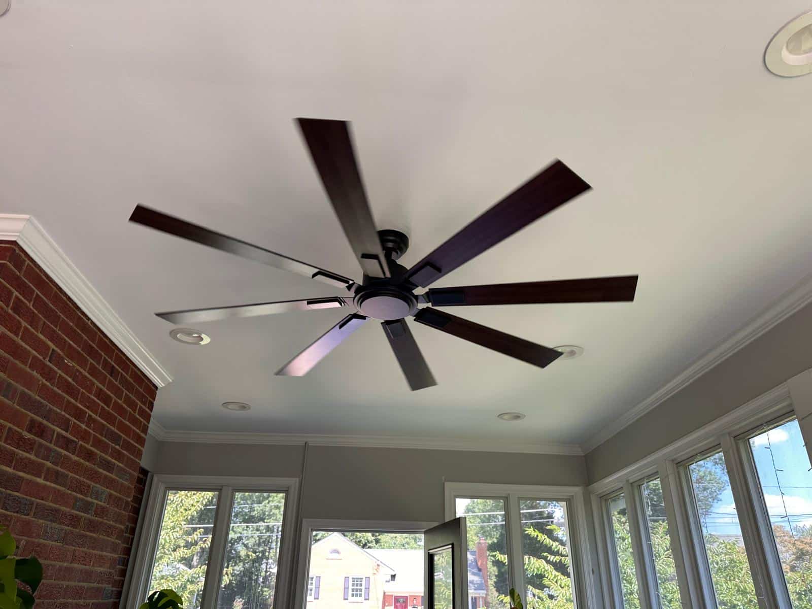 New dark 8-blade ceiling fan installed in the same sunroom after replacement