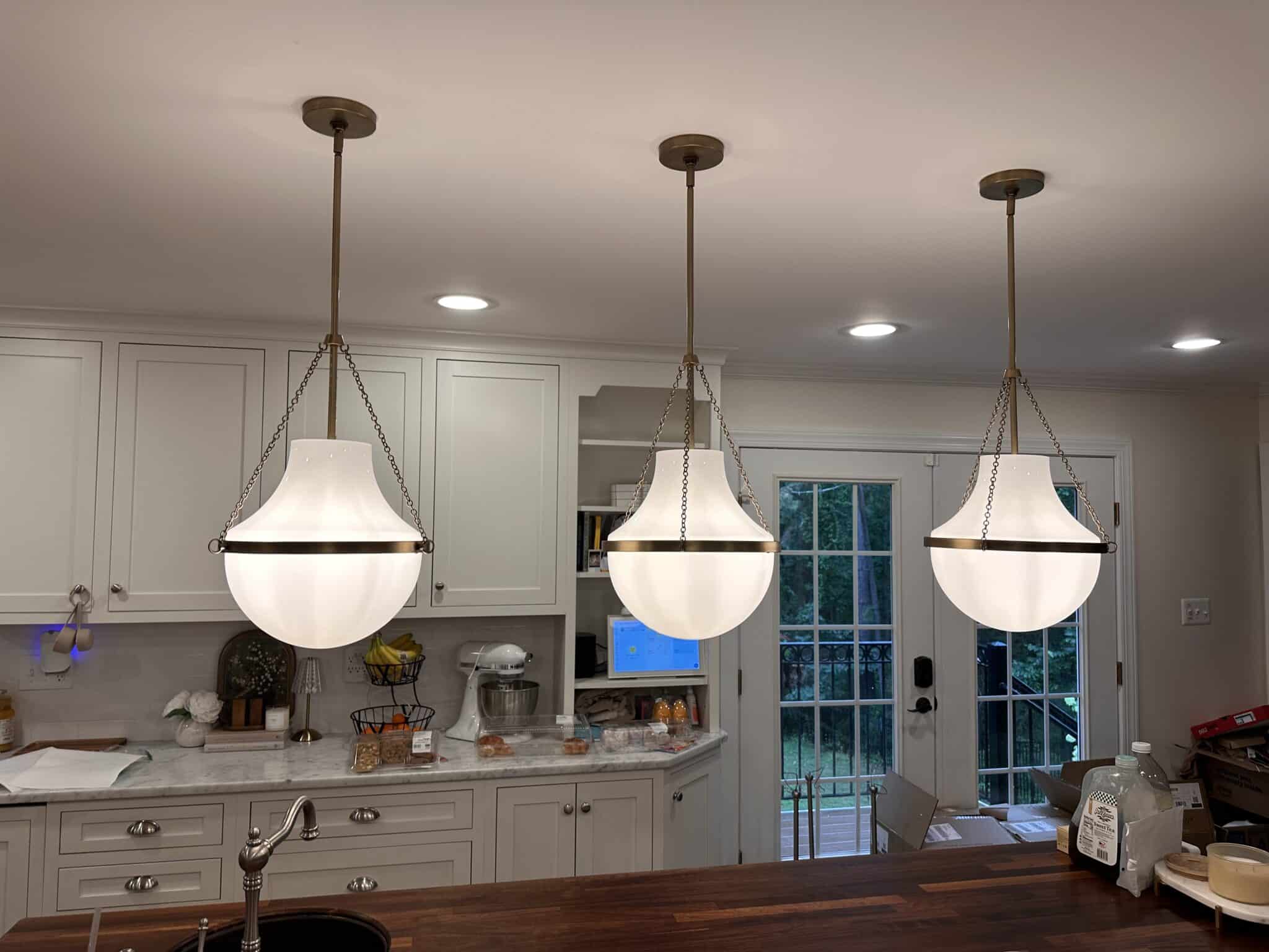 Three pendant globe lights installed over a kitchen island with recessed lights in the ceiling