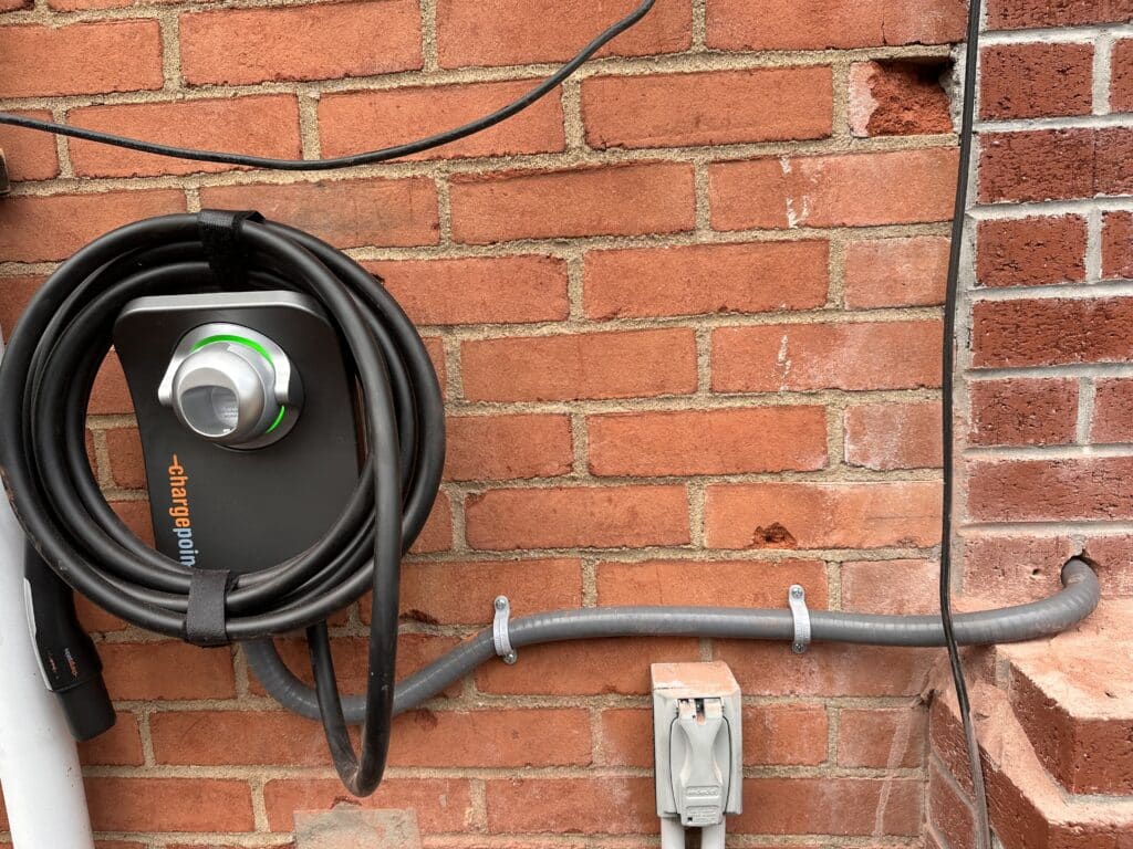 A ChargePoint Level 2 charger on a brick exterior wall, with the conduit run and a weatherproof in-use cover below